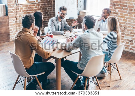 Everyday meeting. Group of six young people discuss something and gesturing while sitting at the table in office