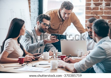 Concentrated at work. Group of five young people discuss something and gesturing while leaning to the table in office