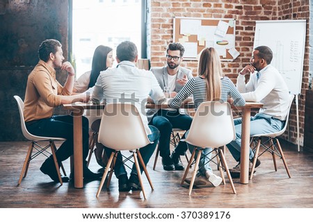 Morning meeting. Group of six young people discussing something while sitting at the table in office together