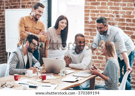 Successful team. Group of cheerful young people discussing something with smile and gesturing while leaning to the table in office