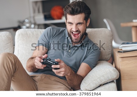 That is my best round! Excited young handsome man playing video game and keeping mouth open while sitting on the couch at home