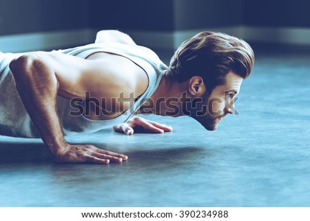 Strength and motivation. Side view of young handsome man in sportswear doing push-up at gym