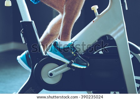 Intense cardio workout. Side view close-up part of young man in sports shoes cycling at gym