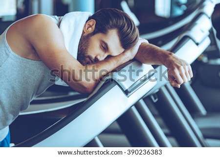 Cannot run anymore. Side view of young man in sportswear looking exhausted while leaning on treadmill at gym