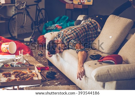 When the party is over. Young handsome man passed out on sofa in messy room after party