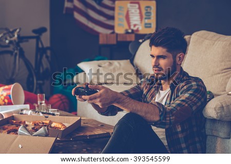 Exhausted gamer. Frustrated young man holding joystick while sitting on the floor in messy room after party