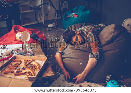 Comfortable place to pass out. Young handsome man passed out on bean bag with joystick in his hand in messy room after party