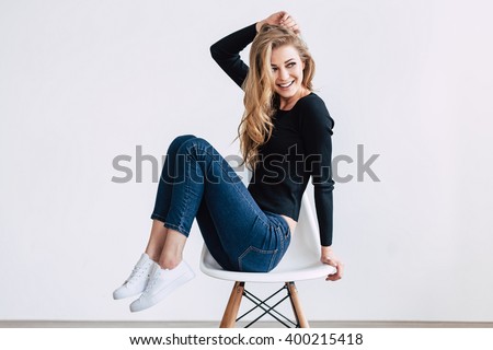 She is simply gorgeous. Beautiful young woman posing and looking away with smile while sitting on chair against white background