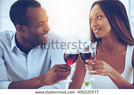 Celebrating their special date. Beautiful young African couple sitting close to each other and holding wineglasses