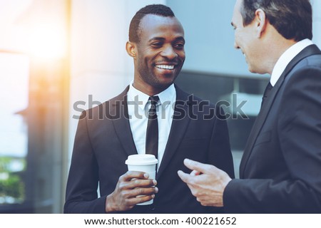 Coffee break. Two cheerful business men talking while one of them holding coffee cup