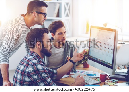 Discussing new project. Three young business people discussing something while looking at the computer monitor together