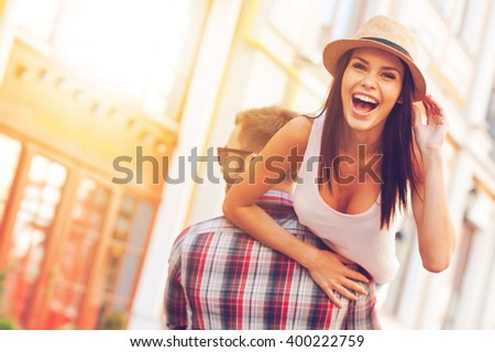 Enjoying beautiful day. Rear view of young cheerful man carrying his beautiful girlfriend on shoulder while walking by the street