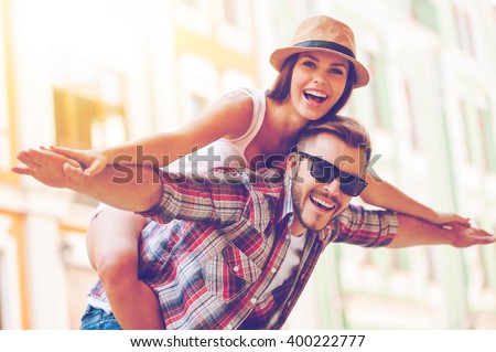 Happy to be together. Happy young man piggybacking his girlfriend while keeping arms outstretched