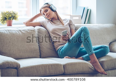Resting with joy. Beautiful young woman listening to music and keeping eyes closed while sitting on sofa at home