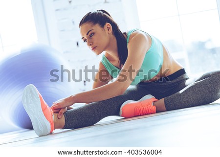 Staying flexible. Young beautiful woman in sportswear doing stretching while sitting on the floor in front of window at gym