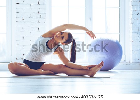 Beautiful and flexible. Young beautiful young woman in sportswear doing stretching while sitting in front of window at gym