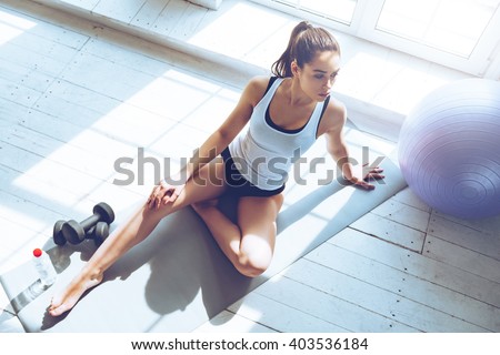 Relaxing after training. Top view of beautiful young woman looking away while sitting on exercise mat at gym