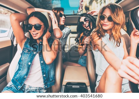 Driving with friends is always fun! Four beautiful young cheerful women looking happy and playful while sitting in car
