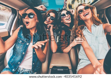 Having fun together. Four beautiful young cheerful women looking happy and playful while sitting in car