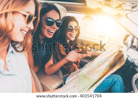 Adventure begins right now! Side view of three beautiful young cheerful women looking away with smile while sitting in car