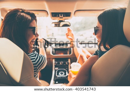 Perfect start of holidays. Rear view of two beautiful young cheerful women looking at each other with smile while sitting in car