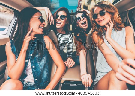 Enjoying road trip together. Four beautiful young cheerful women looking happy and playful while sitting in car