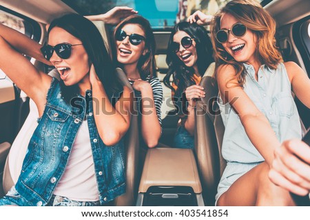 Unstoppable beauties. Four beautiful young cheerful women looking happy and playful while sitting in car