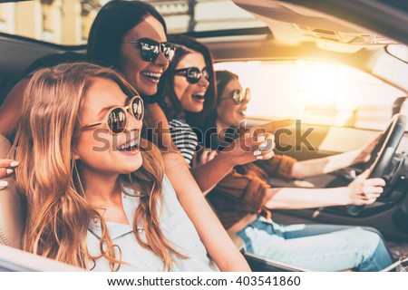 Just keep driving! Side view of four beautiful young cheerful women looking away with smile while sitting in car