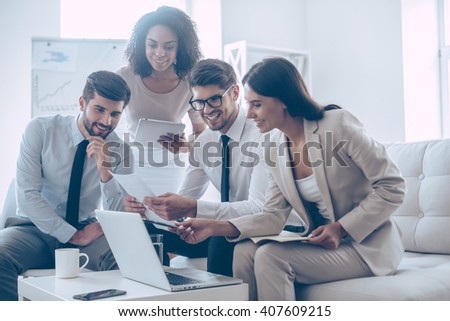 We have great results! Young beautiful woman pointing at her laptop with smile while sitting on the couch at office with her coworkers