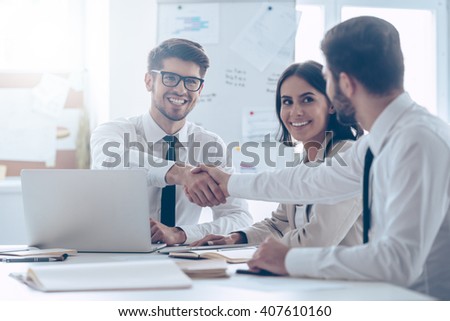 Congratulations! Two handsome man shaking hands with smile while sitting at the office table with their beautiful coworker