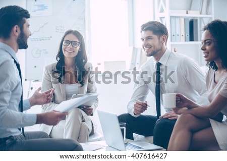 Our work is amazing! Young handsome man holding documents and discussing something with his coworkers with smile while sitting on the couch at office