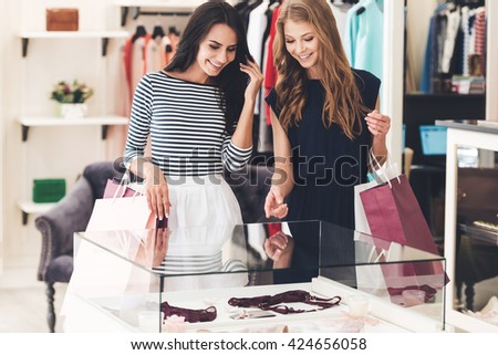 What do you think about this? Two beautiful women with shopping bags looking at lingerie showcase with smile while standing at the store