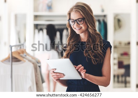 Starting new business. Beautiful young woman using digital tablet with smile while standing at the clothing store