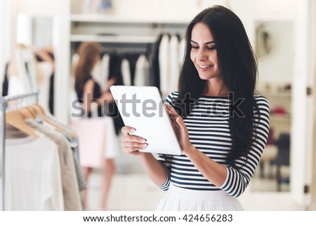 Technologies make business easier. Beautiful young woman using her digital tablet with smile while standing at the clothing store
