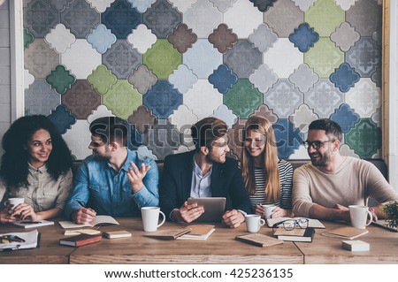Great business meeting. Cheerful young people looking at each other with smile while sitting at the office table on business meeting