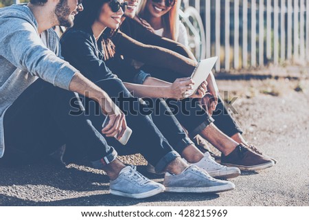 Carefree time with best friends. Close-up of group of young smiling people bonding to each other and looking at digital tablet while sitting outdoors together