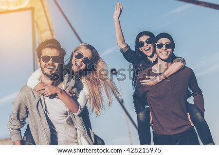Just having fun. Two handsome young men piggybacking their girlfriends and smiling while walking along the bridge