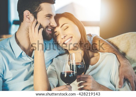 Love is a in the air. Beautiful young loving couple sitting close to each other and drinking red wine