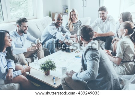 Welcome to team! Group of confident business people sitting around the desk together while two men shaking hands and smiling