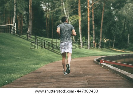 Starting day from morning jog. Full length rear view of young man in sports clothing jogging in park