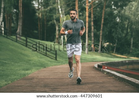 Starting day from morning jog. Full length of handsome young man in sports clothing jogging in park