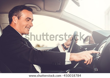 Driving with pleasure. Side view of cheerful mature man in formalwear driving car and touching dashboard with finger