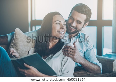 Spending nice time at home. Beautiful young loving couple bonding to each other and smiling while woman holding a book