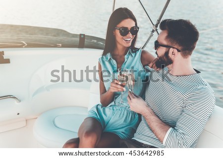 Celebrating love. Smiling young couple holding glasses with champagne and looking at each other while sitting on the board of yacht