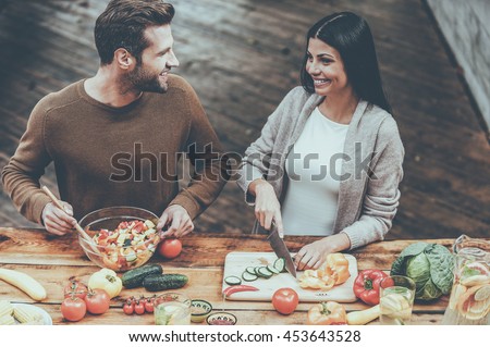 Cooking healthy. Top view of beautiful young couple preparing healthy salad together and smiling