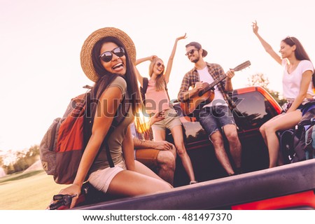 Enjoying road trip with best friends. Group of young cheerful people dancing and playing guitar while enjoying their road trip in pick-up truck together