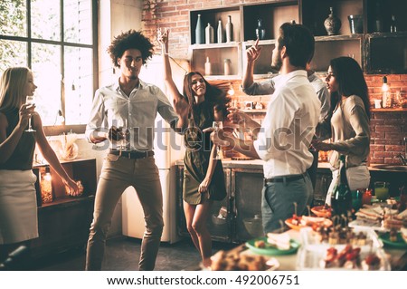Friends dancing. Cheerful young people dancing and drinking while enjoying home party on the kitchen