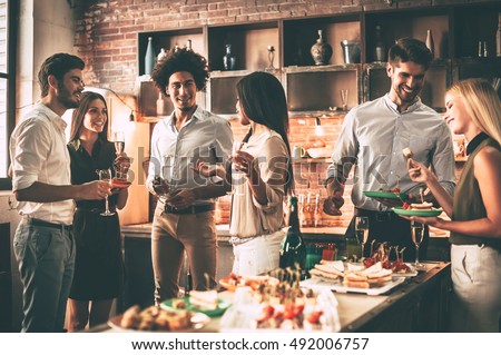 Party with best friends. Group of cheerful young people enjoying home party with snacks and drinks while communicating on the kitchen