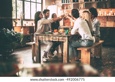Cheers to the best friends! Group of cheerful young people cheering with champagne flutes and looking happy while while sitting at the dinning table together