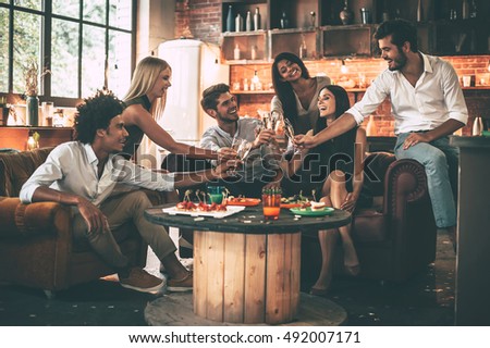 Cheers! Group of cheerful young people enjoying food and drinks while spending nice time in cofortable chairs on the kitchen together